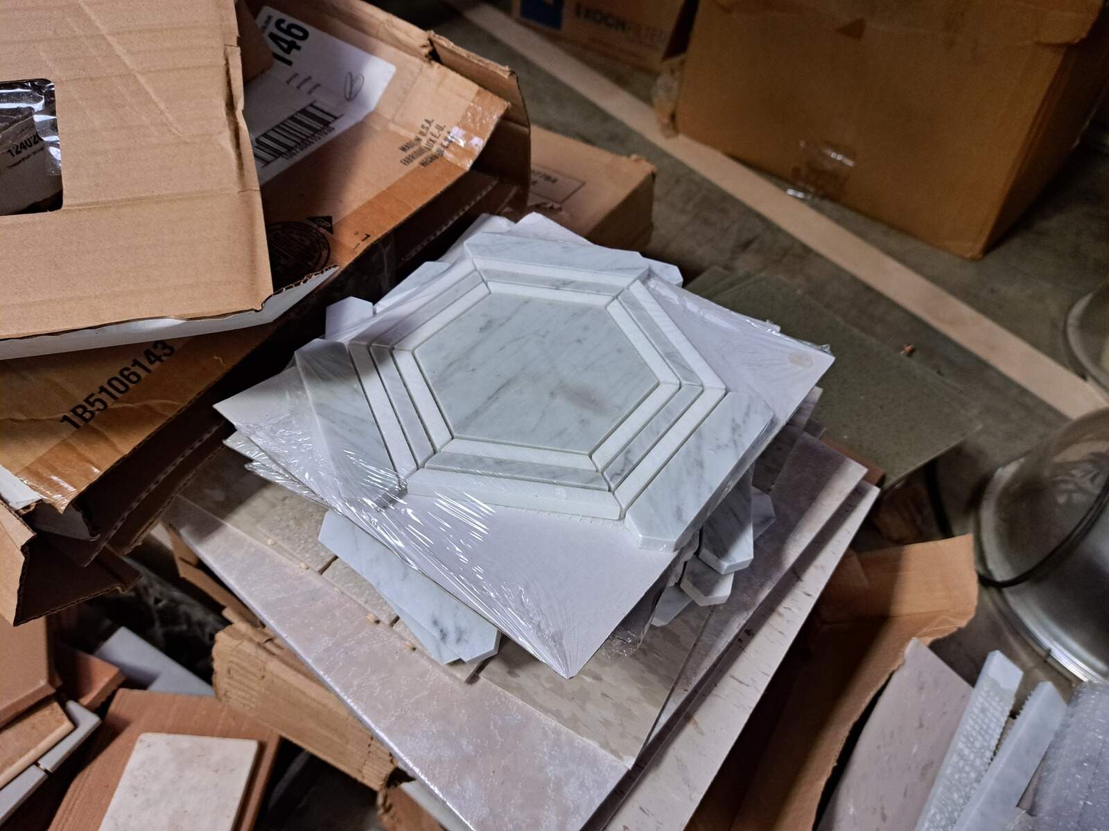 Stack of white marble hexagon trim tiles sitting on top of open cardboard boxes in a warehouse.