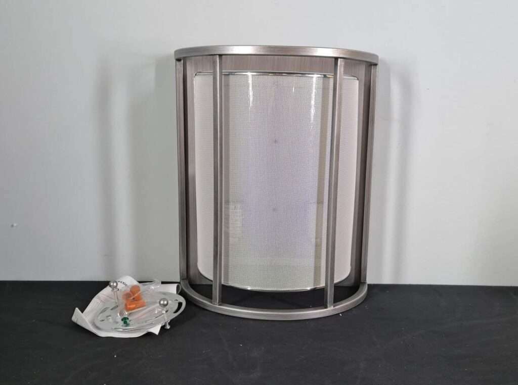 Front view of a brushed nickel cage-style wall sconce with diffuser and included mounting plate and hardware on table.