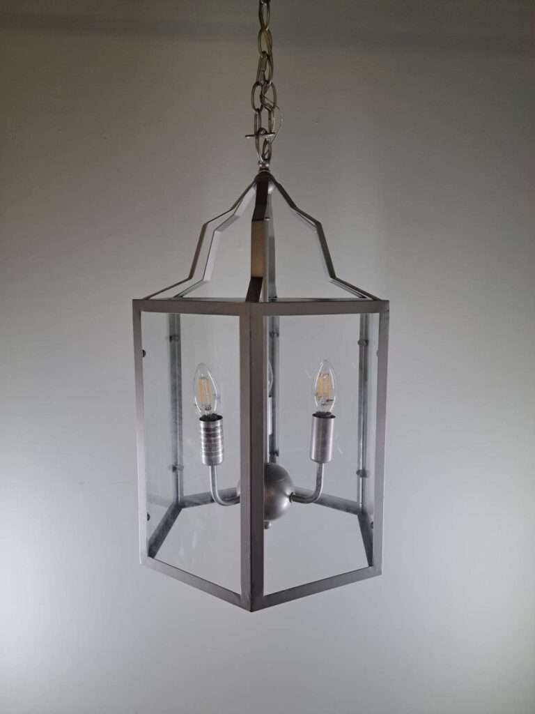 Silver lantern-style foyer pendant hanging from a chain with clear glass panels and three candelabra-style bulbs visible inside.